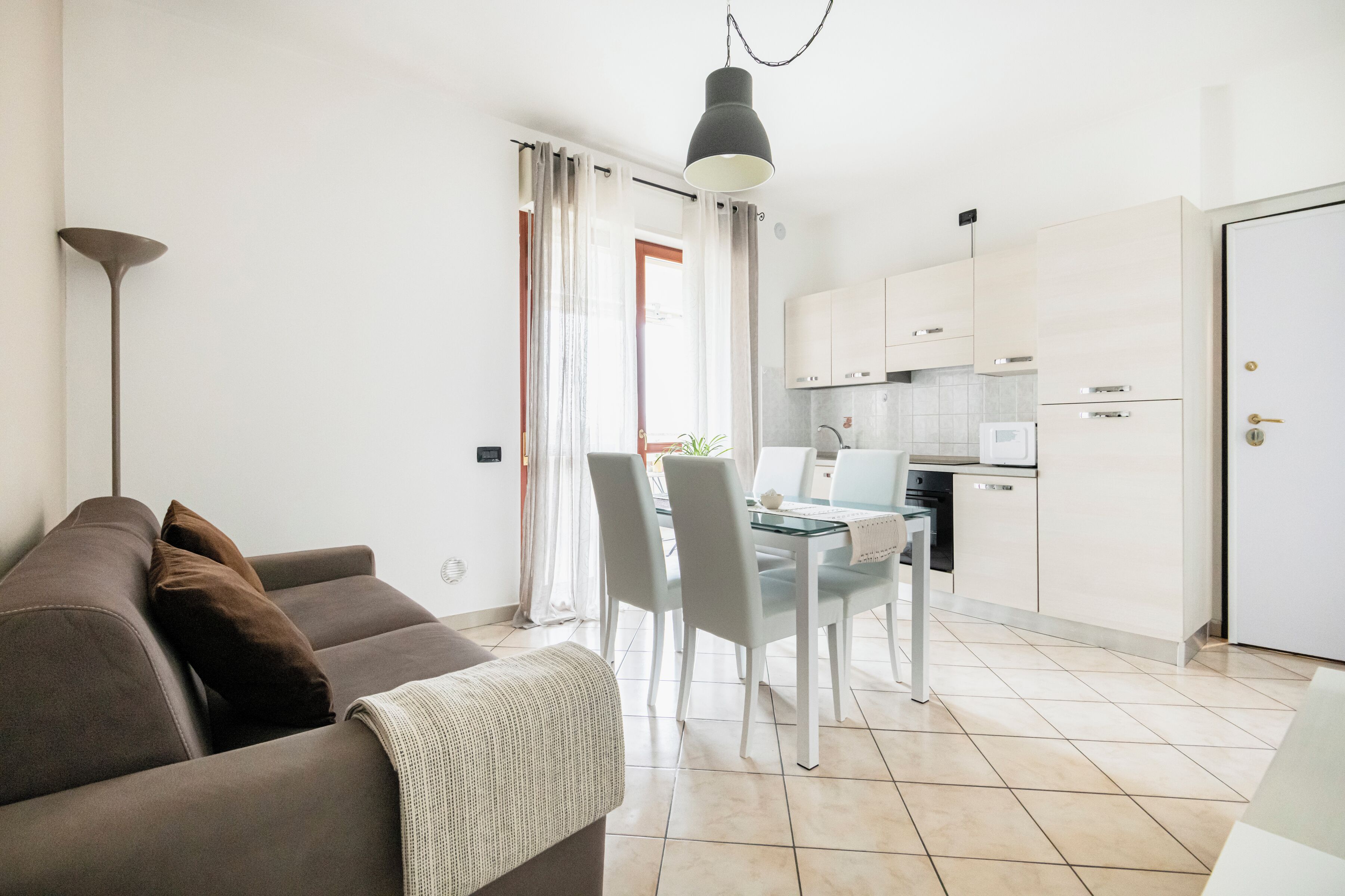 A modern living room with a sofa and a dining table with chairs. There is a kitchen area with cabinets and appliances.
