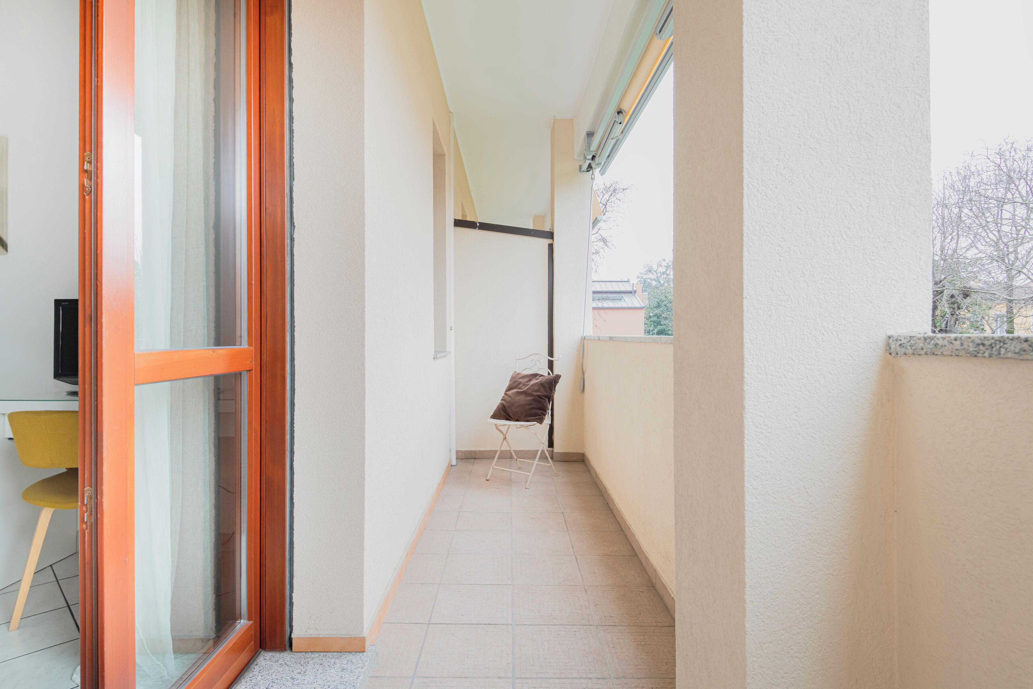Un pasillo estrecho con una puerta de vidrio corredera, una silla y una mesita.