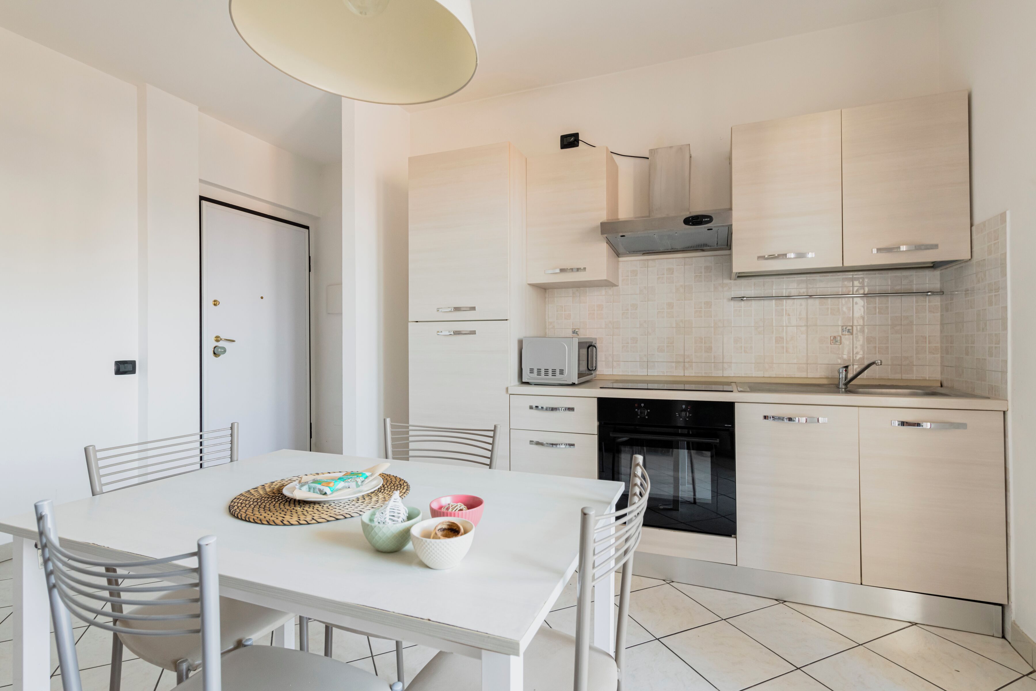 Uma cozinha moderna com armários brancos, uma mesa de jantar com cadeiras e um micro-ondas.