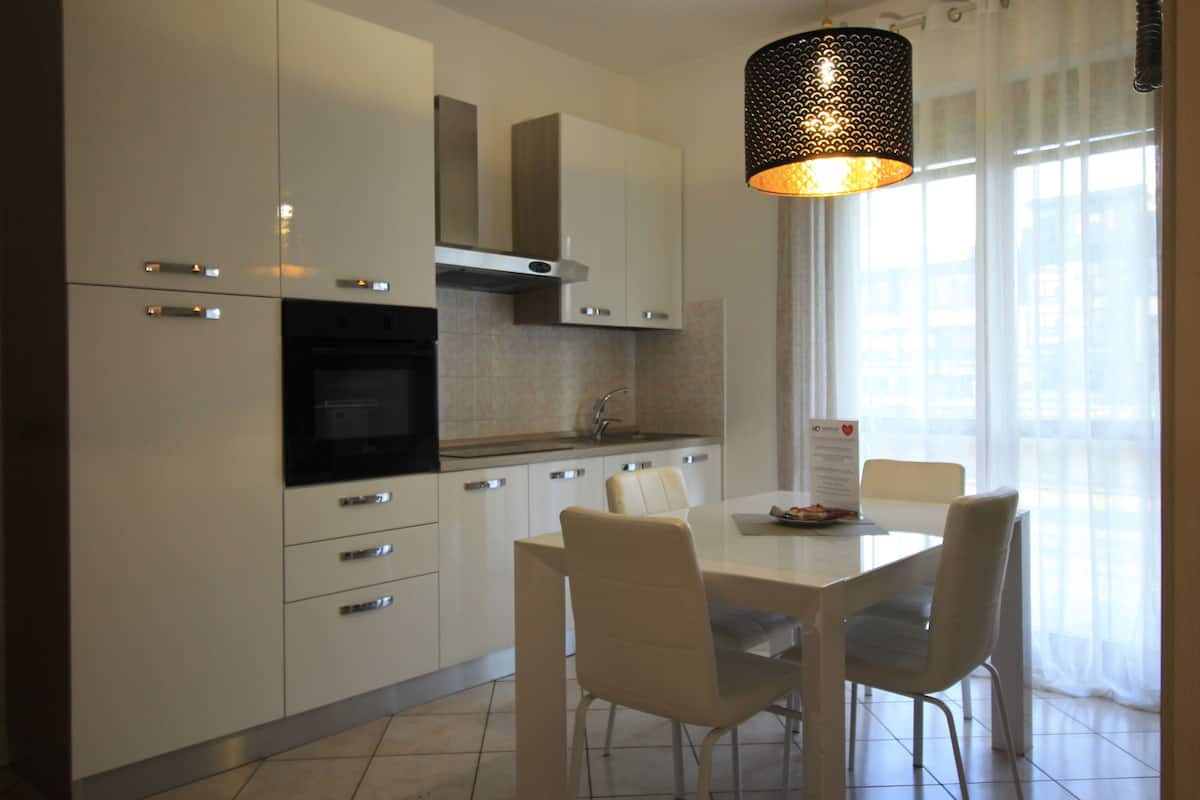A modern kitchen with white cabinetry, a built-in oven, and a dining area with a white table and chairs.