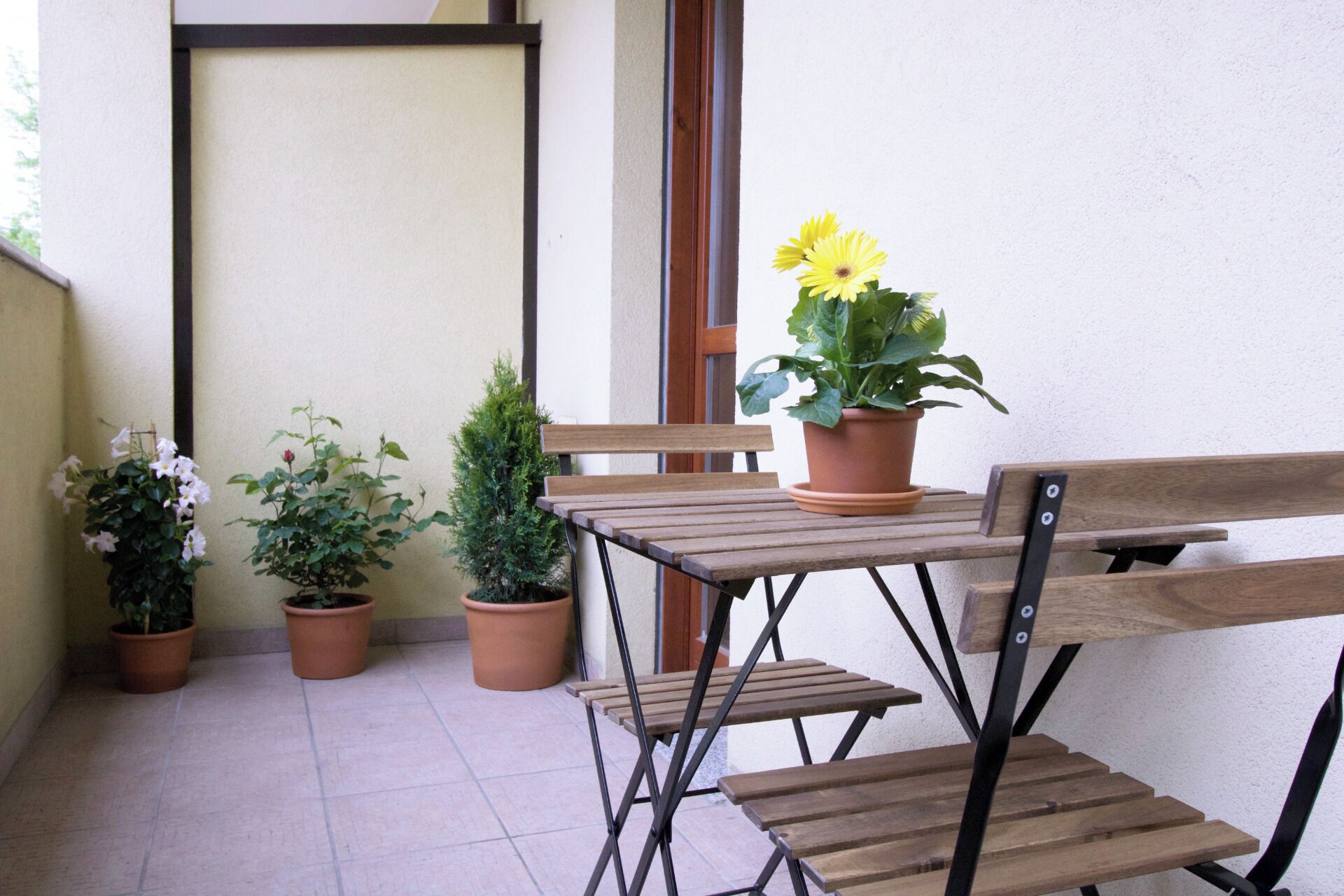 A small outdoor seating area with a wooden table and benches, surrounded by potted plants.