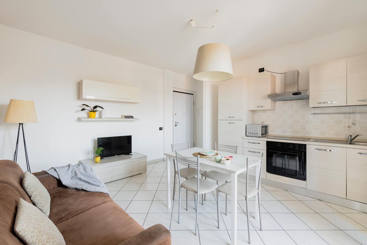 A modern kitchen with white cabinets, a dining table with chairs, a TV, and a lamp.