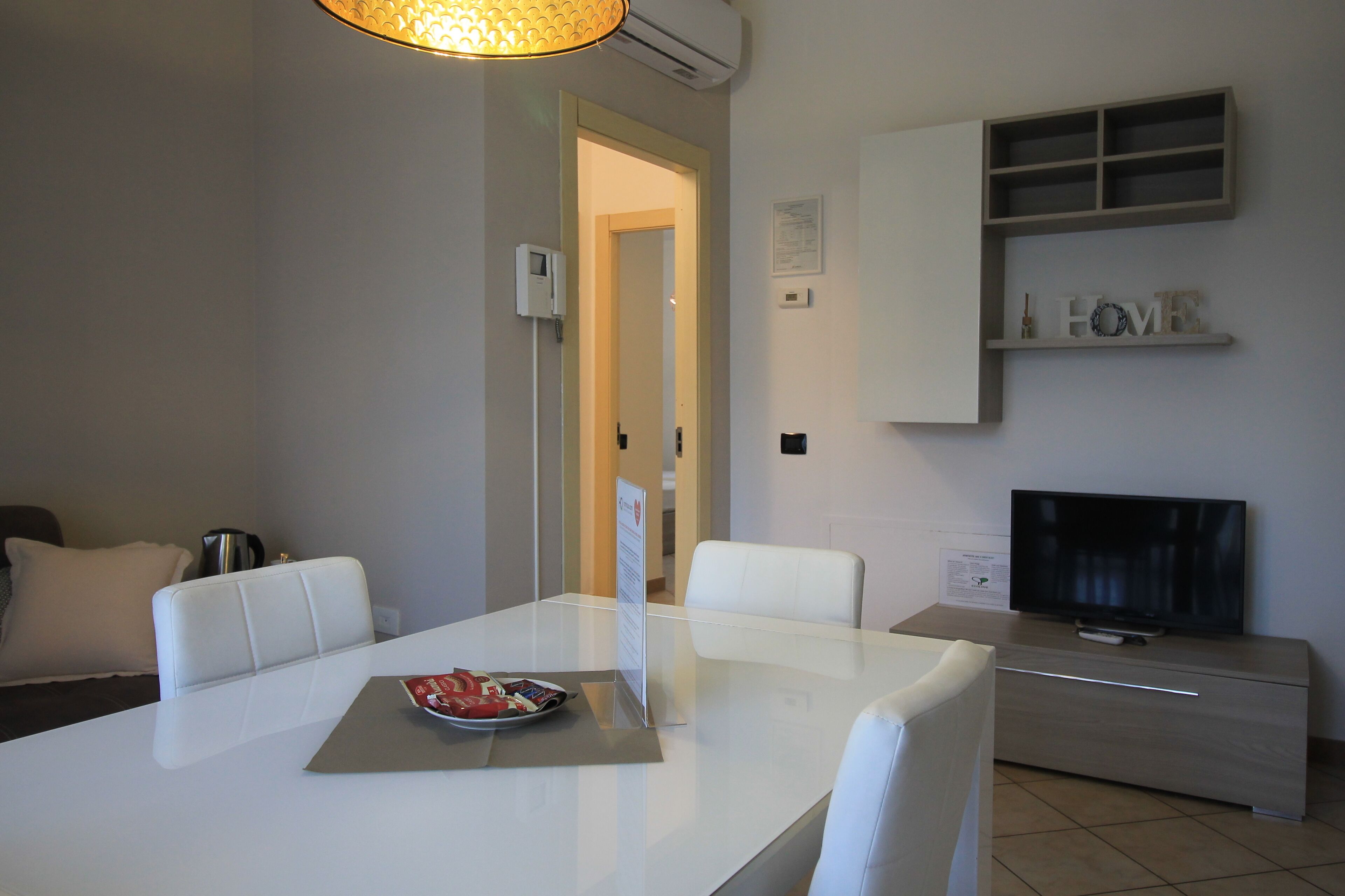 Een moderne woonkamer met een witte eettafel, witte stoelen, een flatscreen-tv en een inbouwkast.