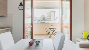 A modern room with a dining area, a small table with chairs, and a view of a balcony with a table and chairs outside. - HQ Aparthotel Milano Inn - Smart Suites (Cinisello Balsamo)