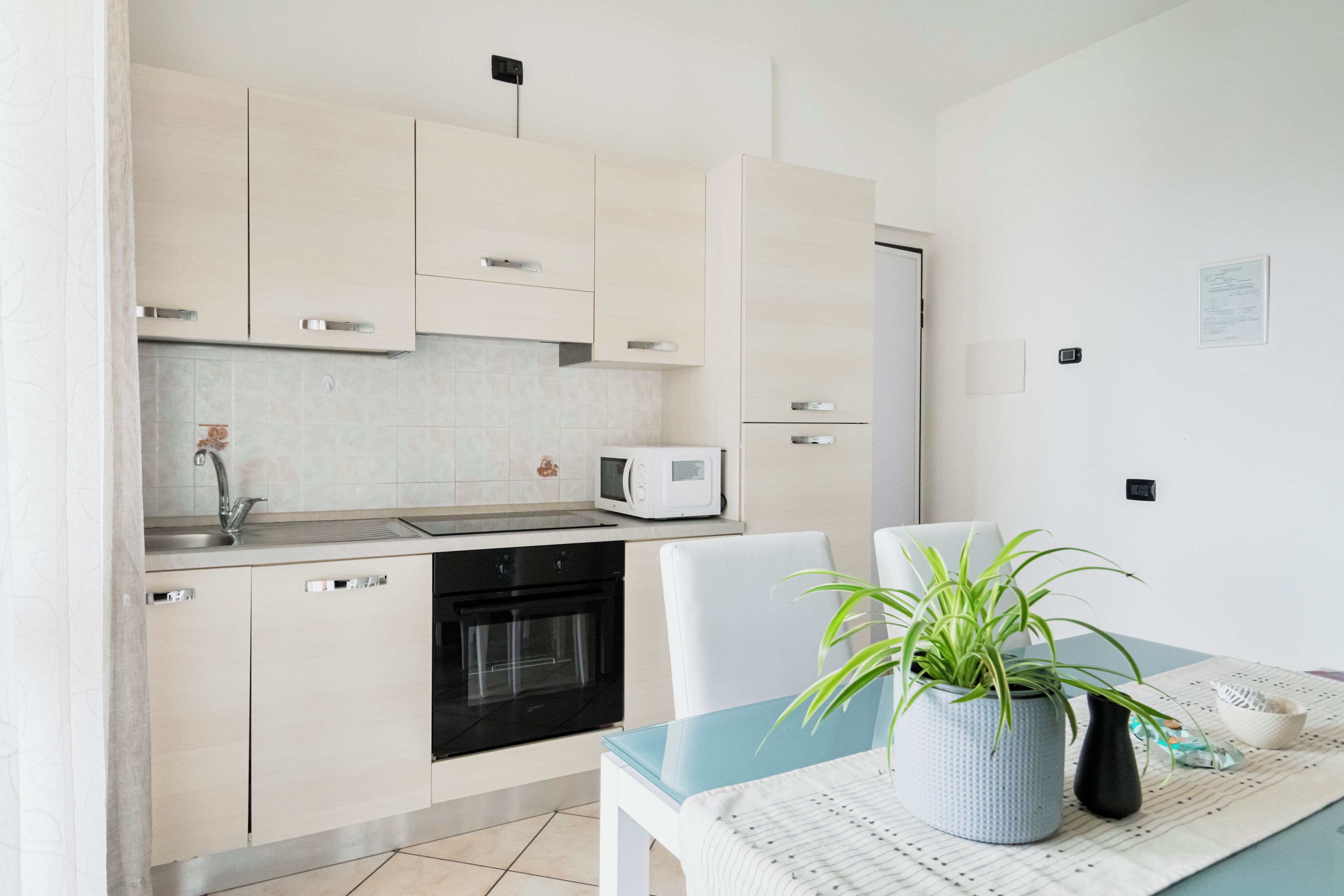 Une cuisine moderne avec des meubles blancs, un four à micro-ondes et un four traditionnel. On y trouve une table avec une plante et un bol.