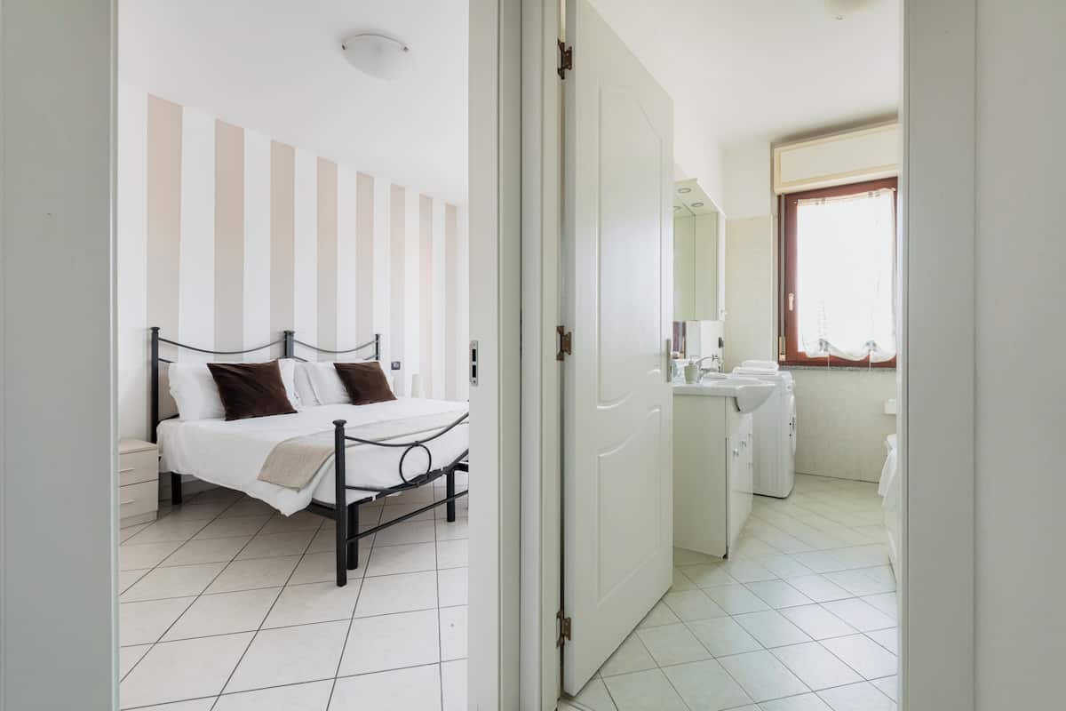A bedroom with a bed, a bedside table, a wardrobe, and a bathroom with a sink and mirror.