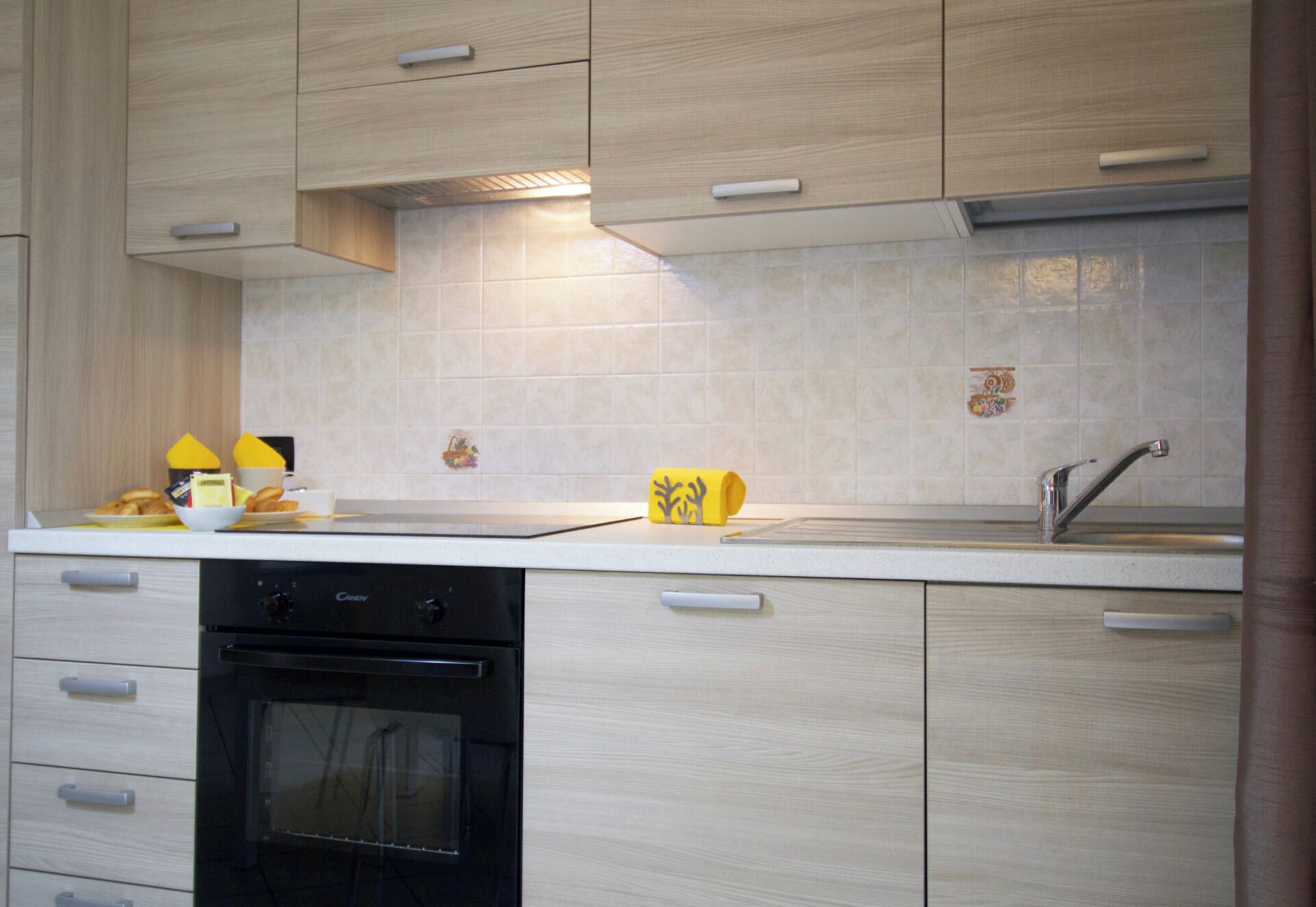 A modern kitchen with light wood cabinetry, a white countertop, and a black dishwasher.