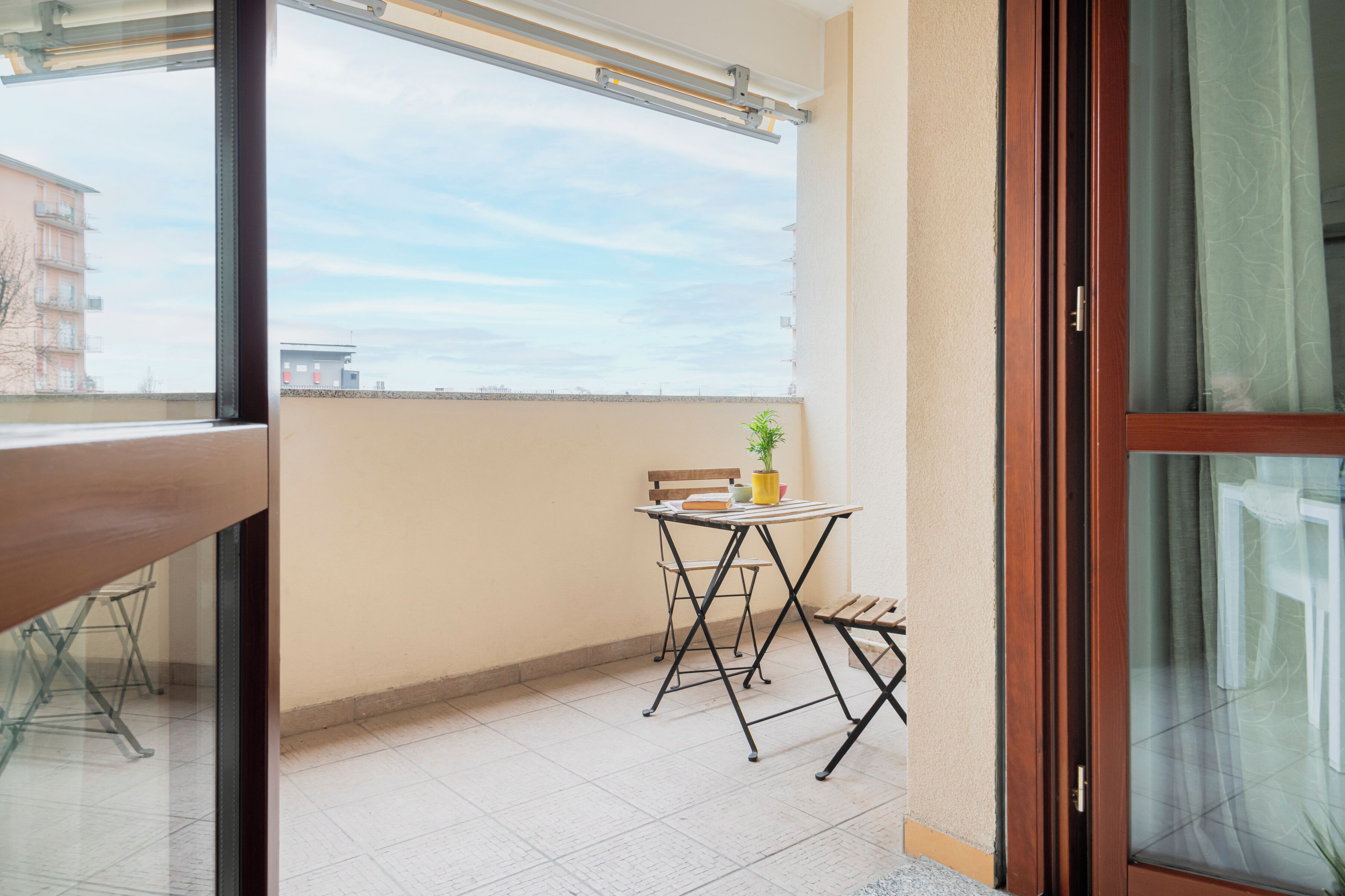 A balcony with a table, chairs, and a potted plant.