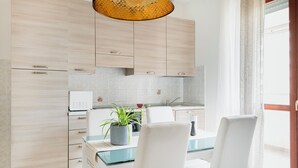 A modern kitchen with light wood cabinets, a glass dining table, white chairs, and a potted plant. - HQ Aparthotel Milano Inn - Smart Suites (Cinisello Balsamo)