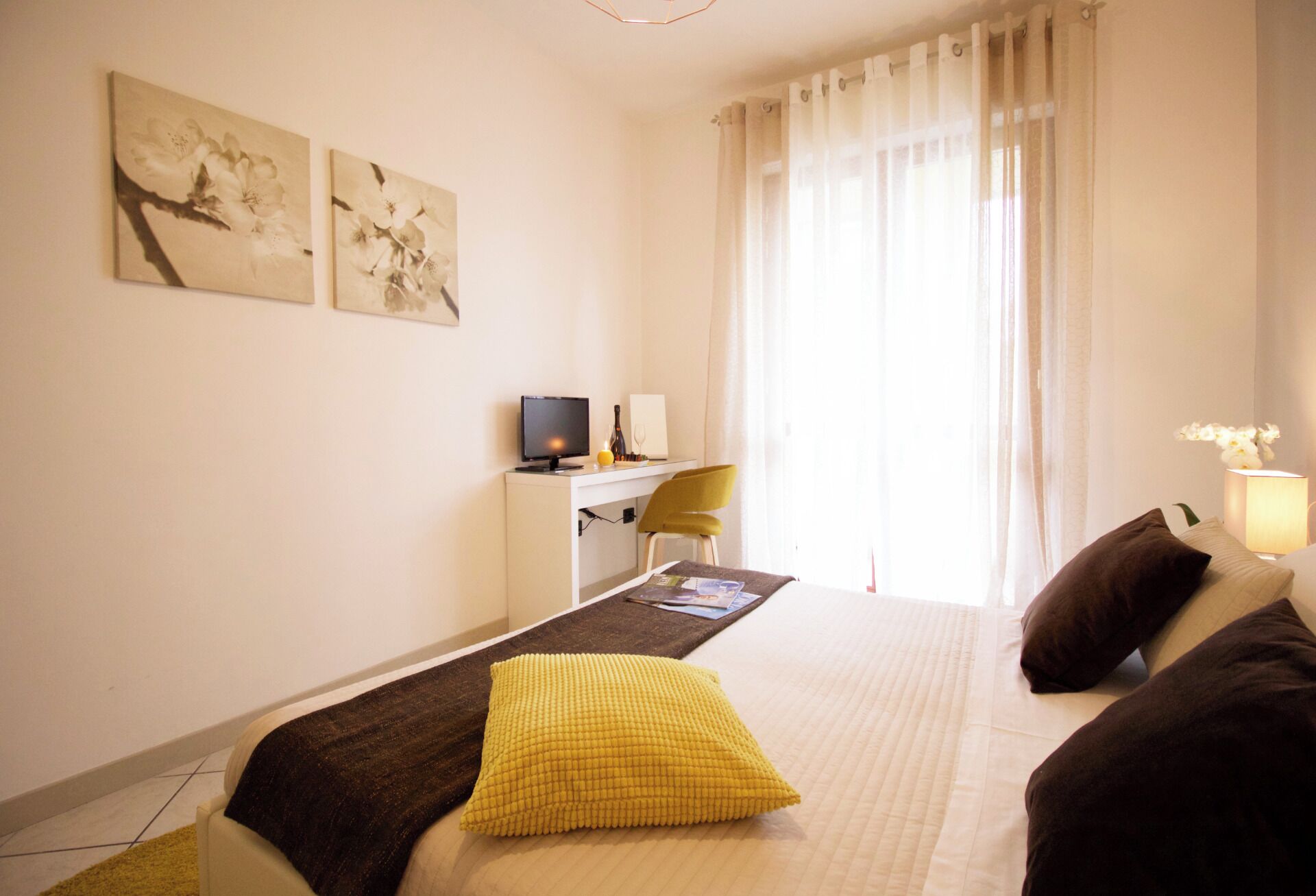 Une chambre d’hôtel avec un lit, un bureau équipé d’un ordinateur, une chaise et des œuvres d’art accrochées au mur.