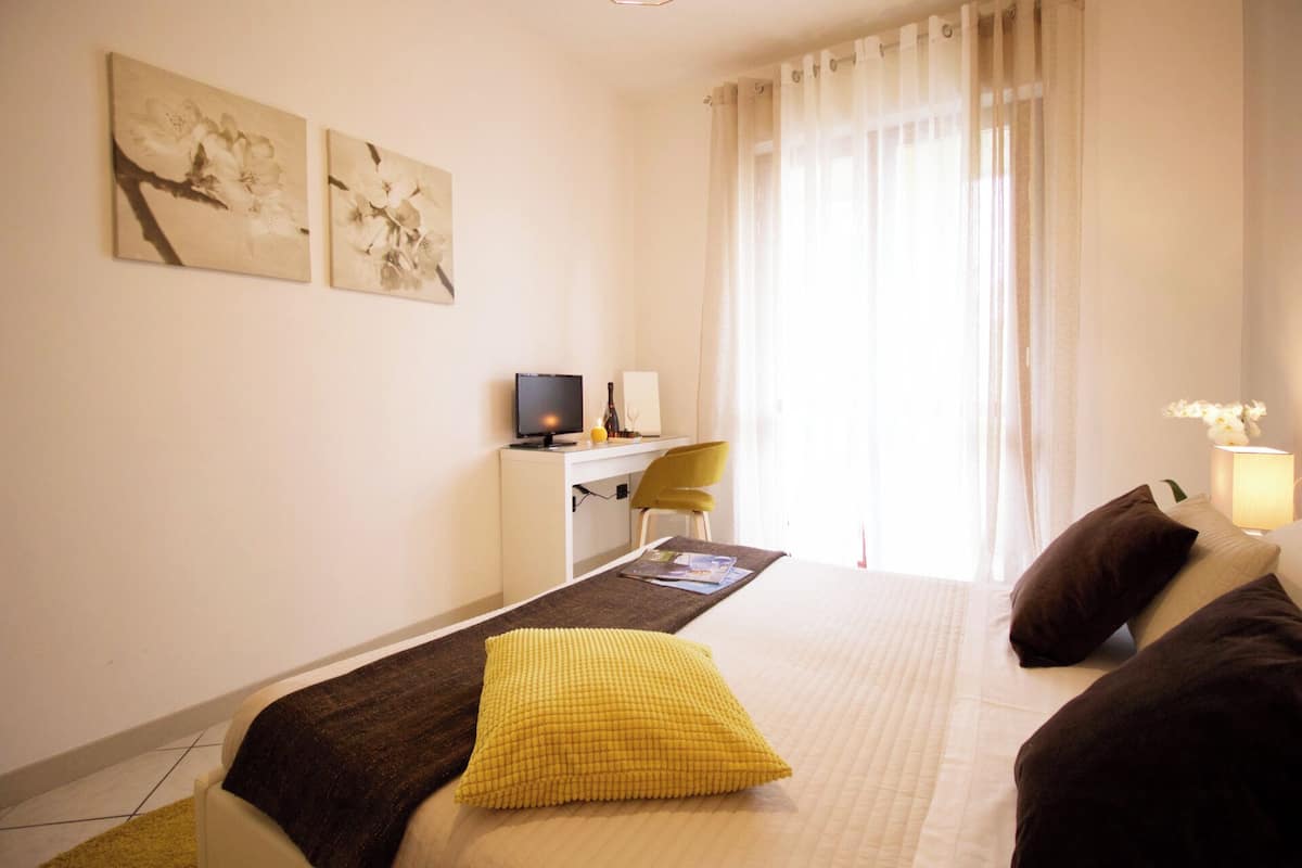 A hotel room with a bed, a desk with a computer, a chair, and artwork on the wall.