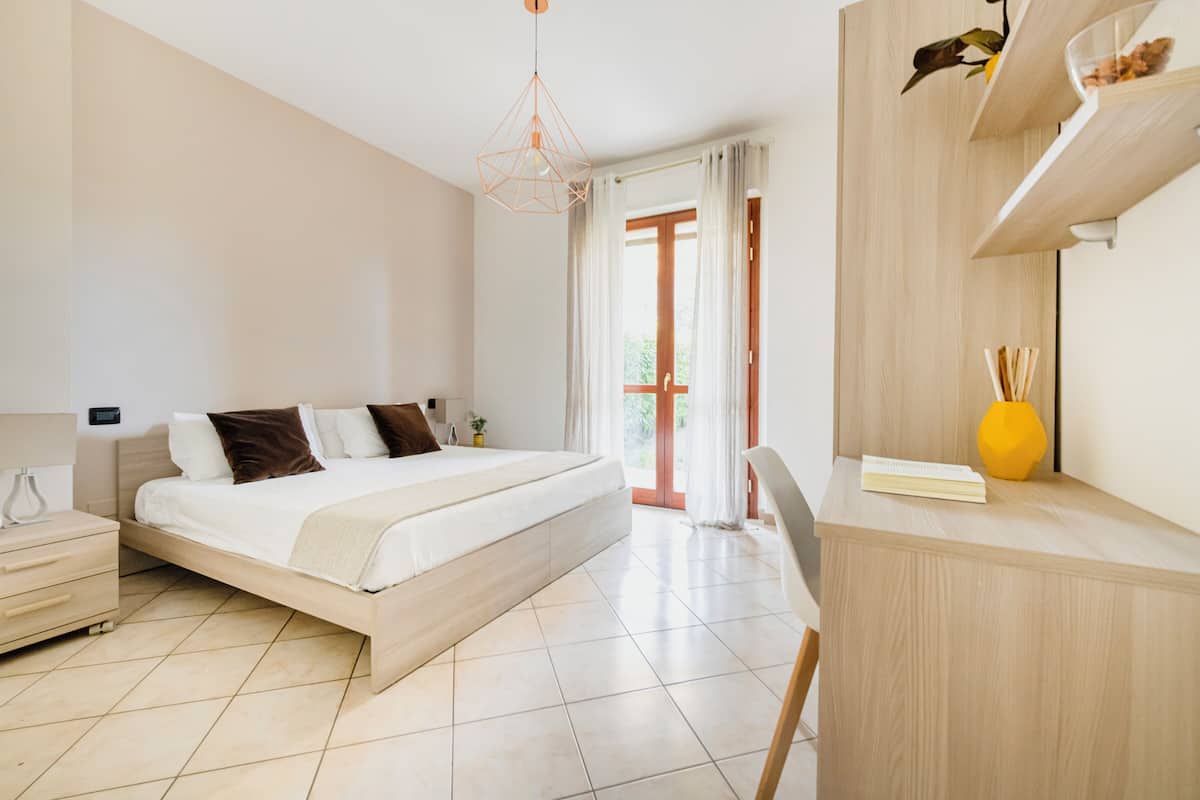 A modern bedroom with a large bed, bedside tables, a desk, and a chair.