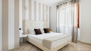 A modern hotel room with a large bed, a bedside table, a lamp, and a view of the outdoors through sheer curtains. - HQ Aparthotel Milano Inn - Smart Suites (Cinisello Balsamo)
