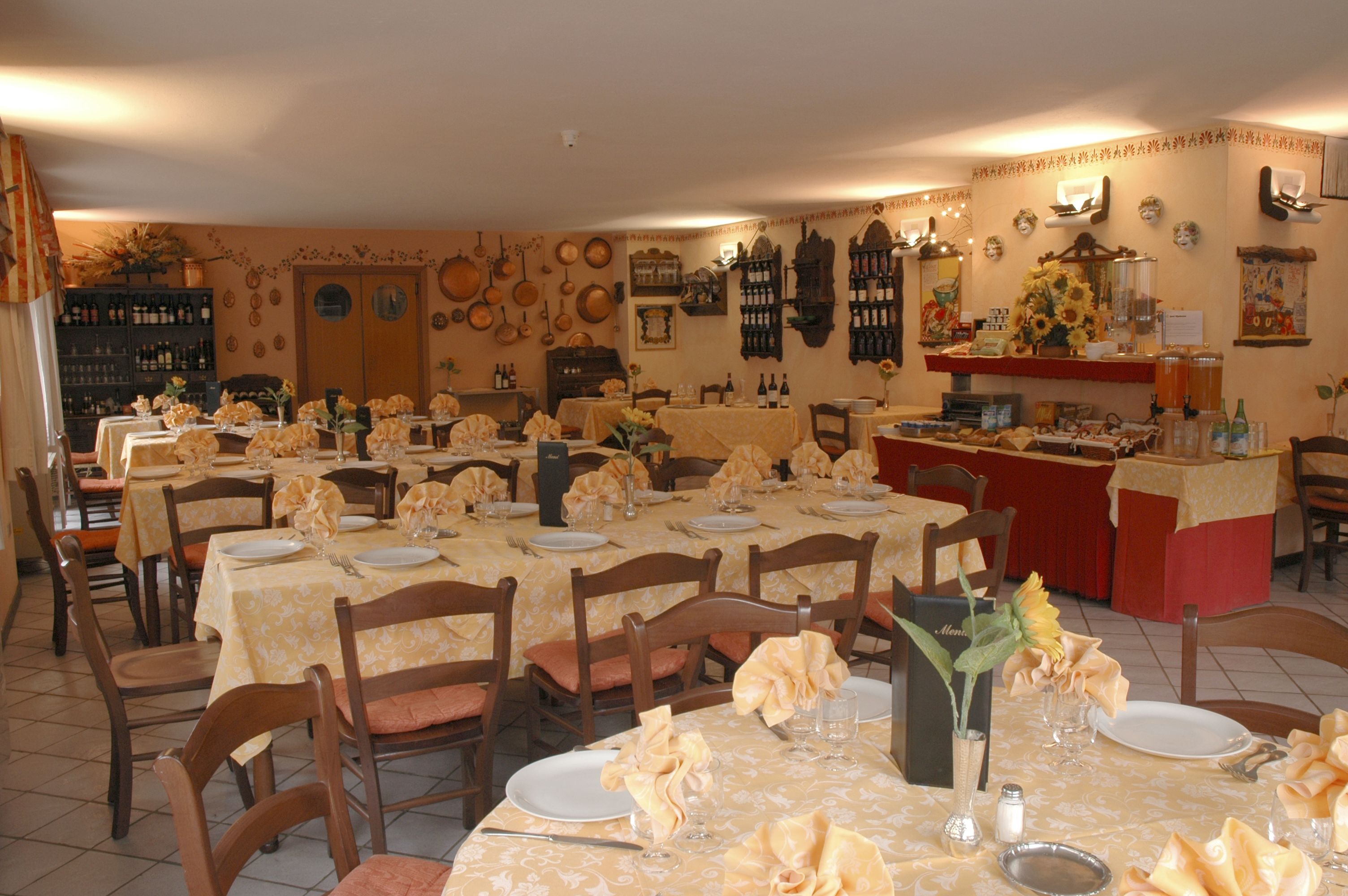 Comedor con varias mesas dispuestas para el servicio, sillas de madera y una variedad de utensilios de cocina y botellas de vino en las paredes.