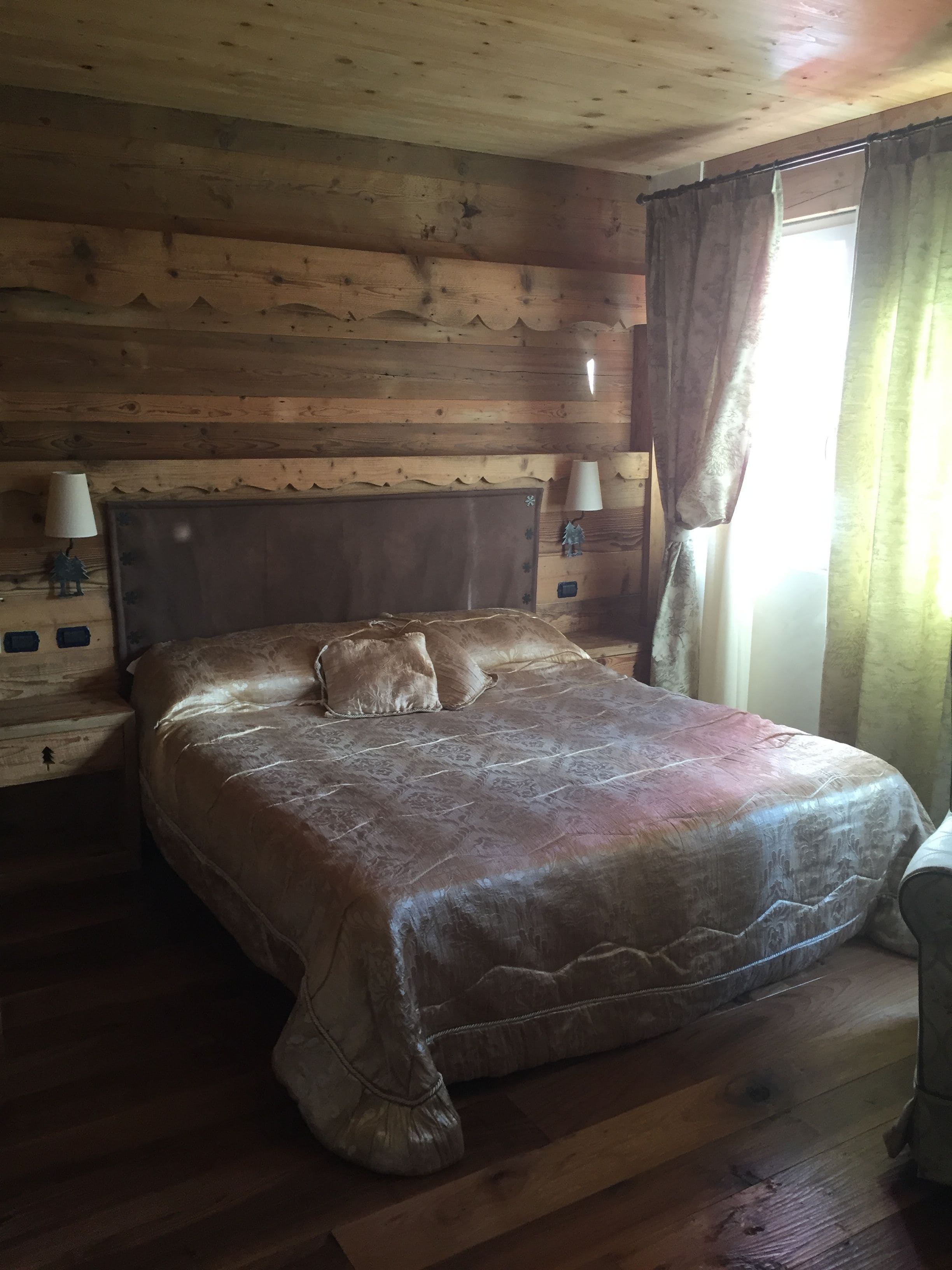 Ett rum inrett som en stuga, med träpanel, en stor säng, två sänglampor och ett fönster med gardiner.