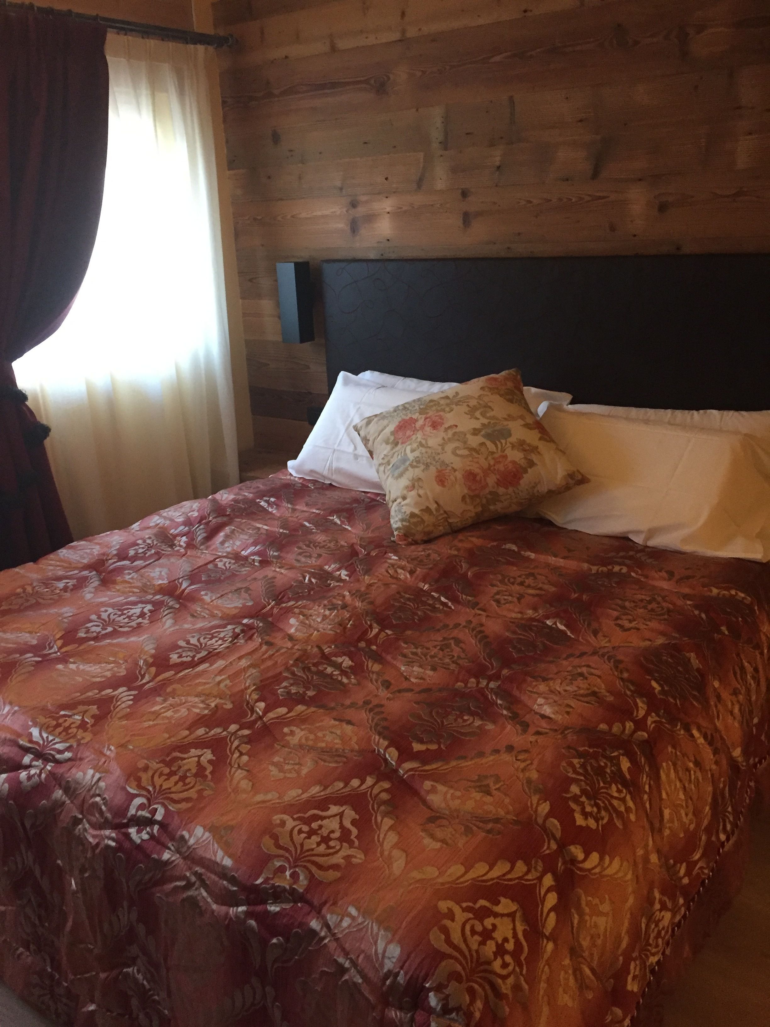 Un lit recouvert d’une couvre-lit à motifs floraux, doté d’une tête de lit sombre et d’une fenêtre agrémentée de rideaux.