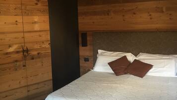 A bedroom with a bed, wooden walls, and a dark-colored pillar.