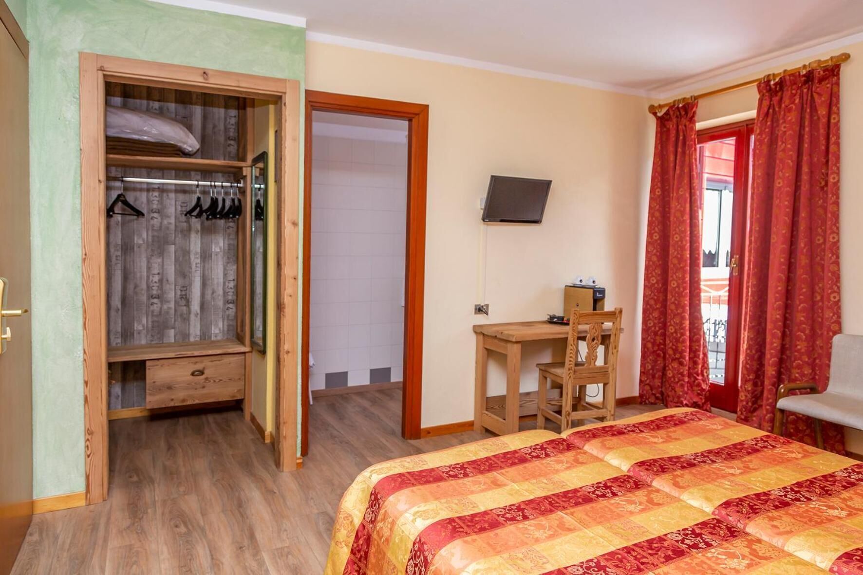 A bedroom with a bed, a desk, a chair, a wardrobe, and a television.