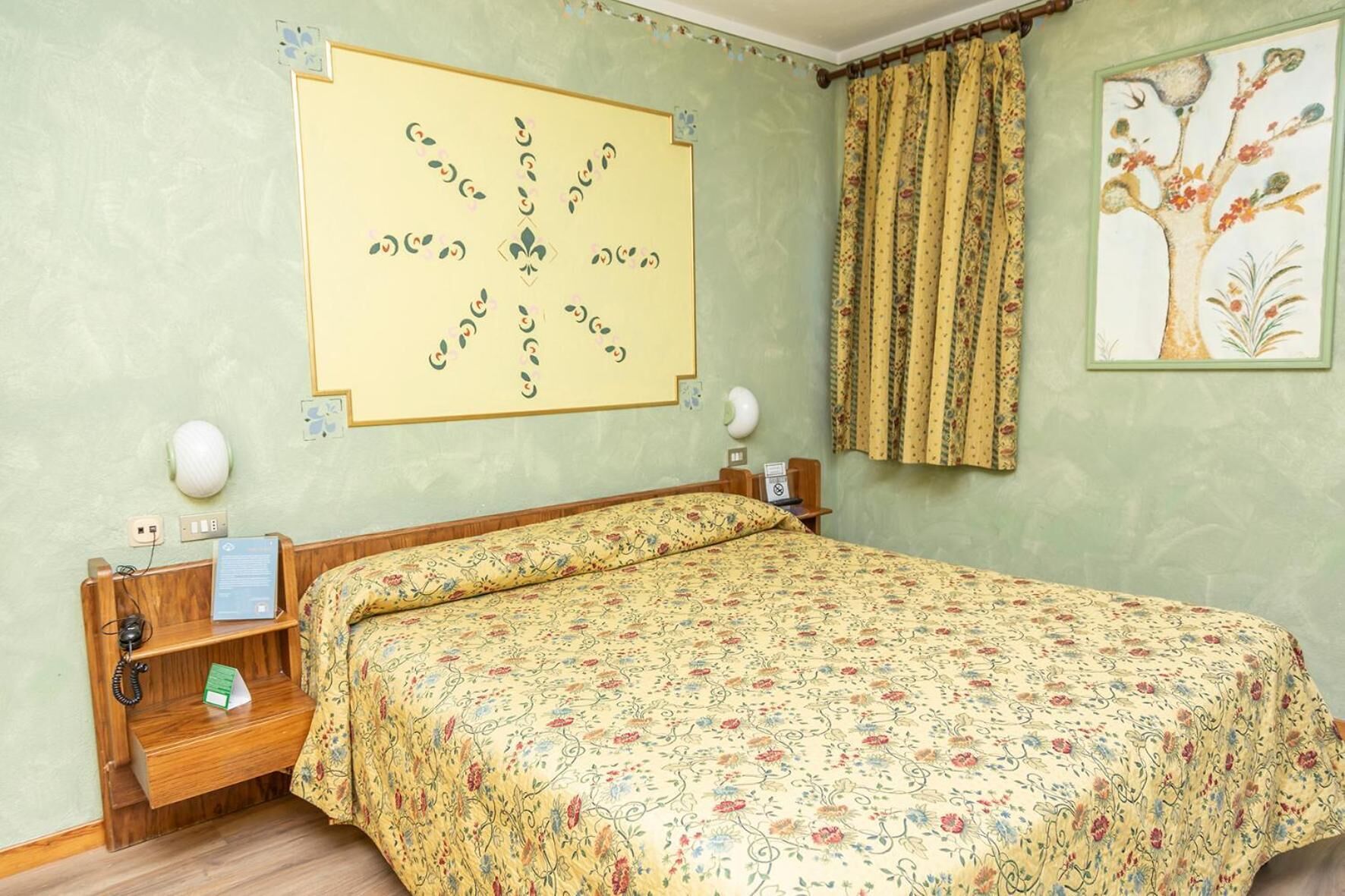 Une chambre à coucher avec une couvre-lit à motifs floraux, une table de chevet en bois avec une lampe et un tableau accroché au mur.