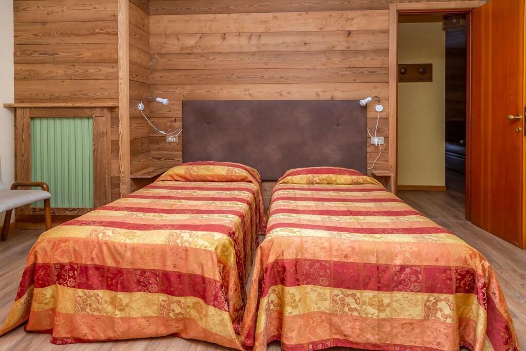 Una habitación tipo cabaña de madera con dos camas, un banco y un radiador verde.