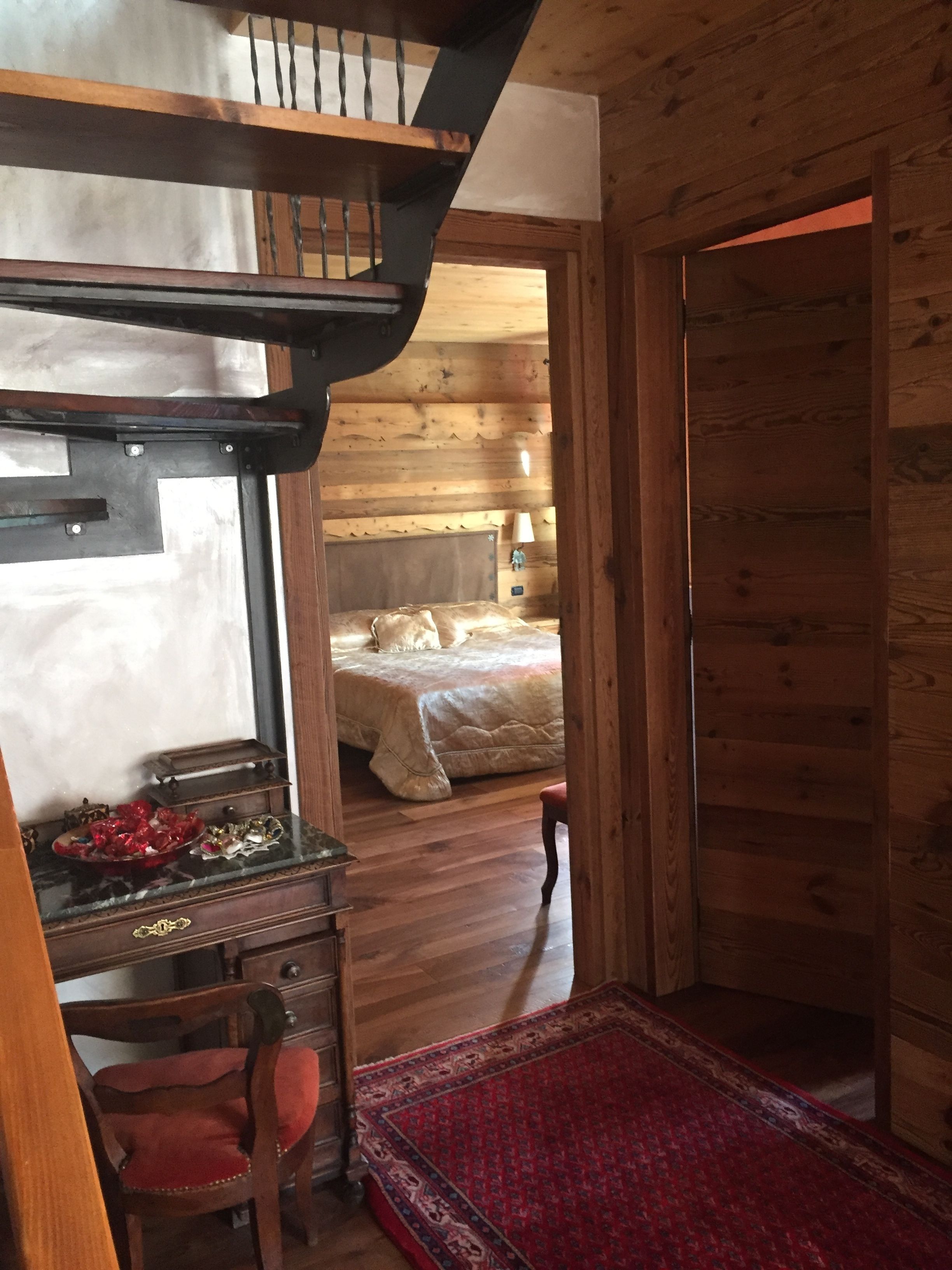 A wooden cabin interior with a bunk bed, a desk with a mirror, and a red rug.