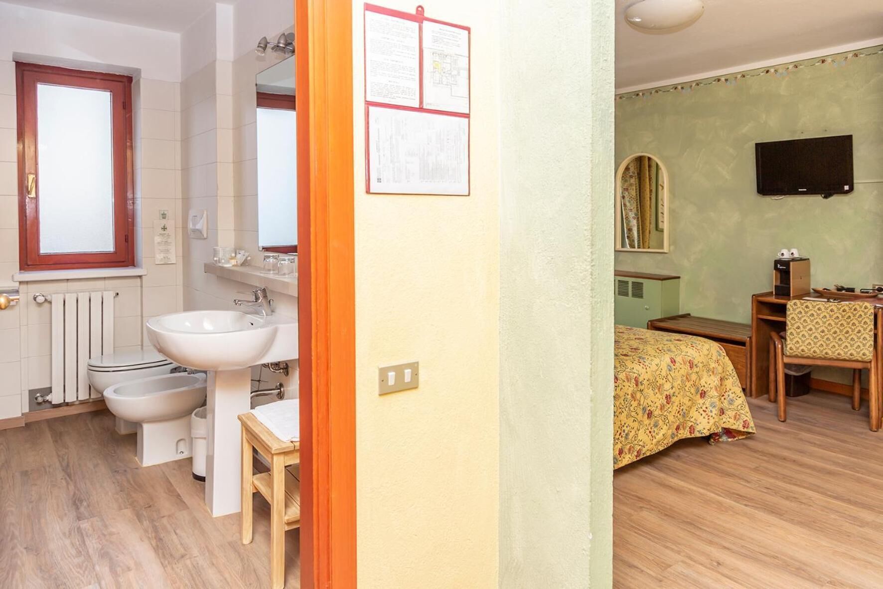 A bathroom with a sink, bidet, and toilet. There is a mirror above the sink and a window with a wooden frame.