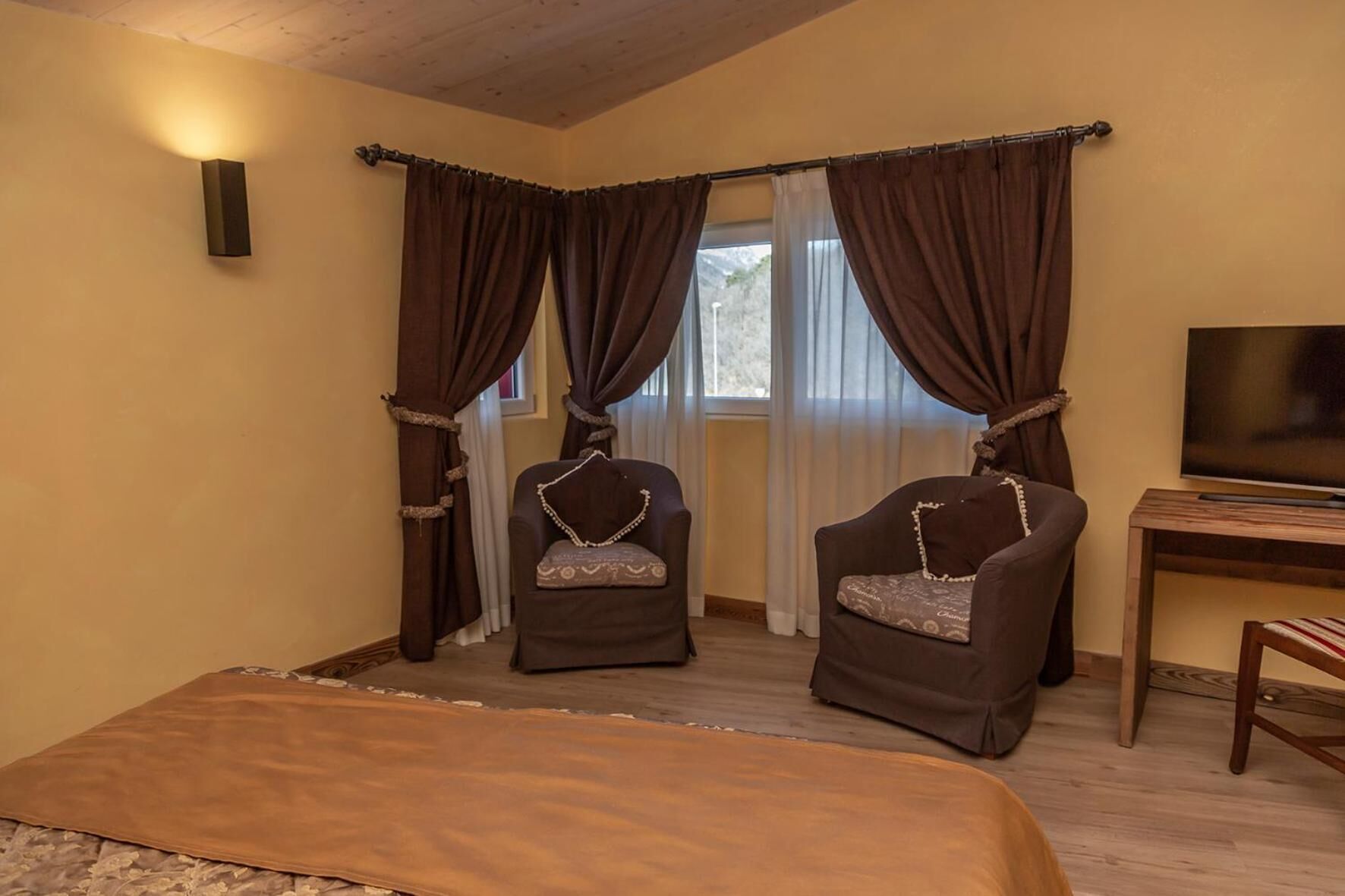 A room with two armchairs, a bed, a TV, and a window with curtains.