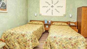 Una stanza con due letti singoli, un armadio in legno, un comodino con una lampada e un quadro appeso al muro.