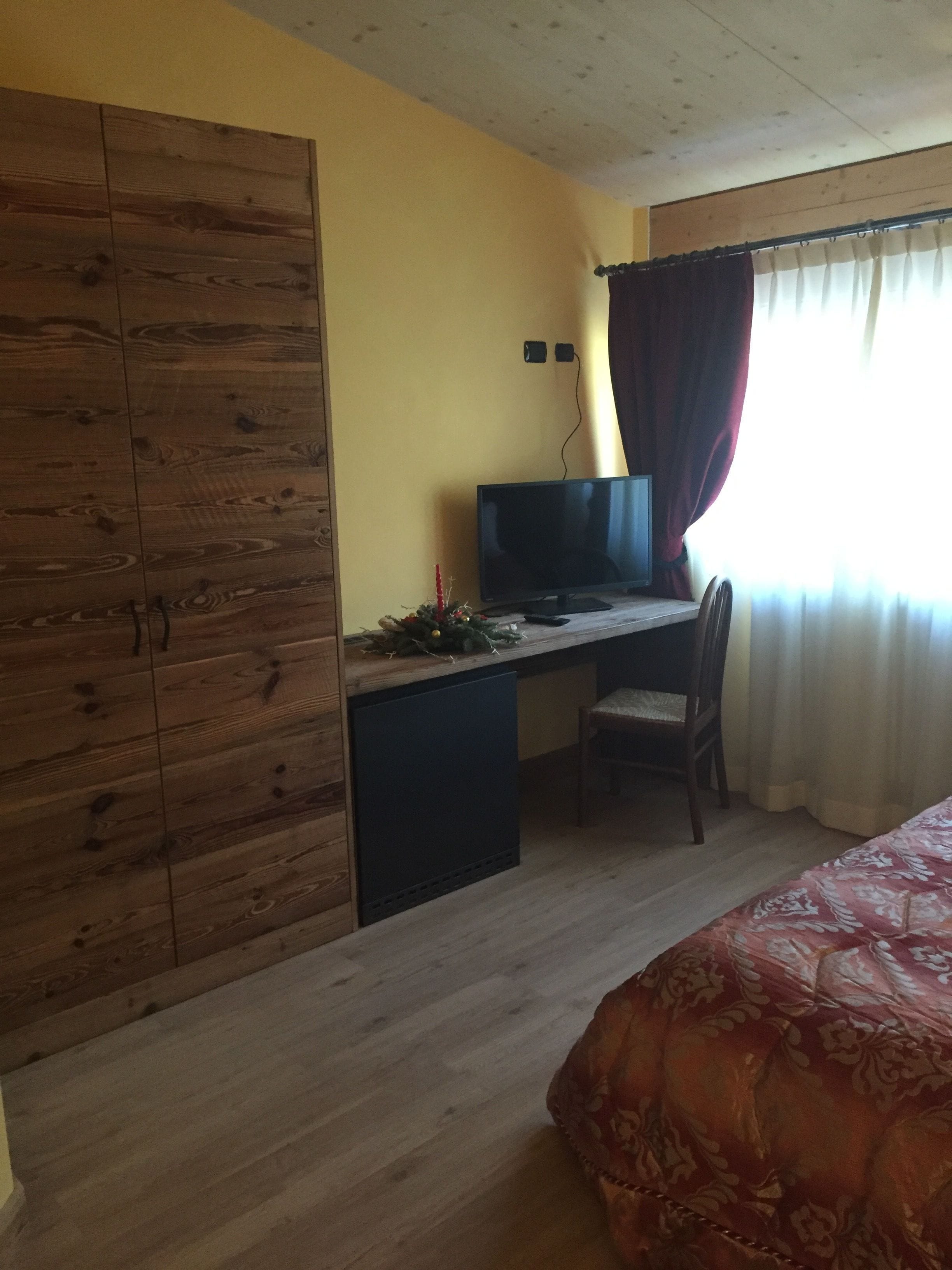 Un dormitorio con un armario de madera, un escritorio con televisor, una silla y una cama con colcha estampada.