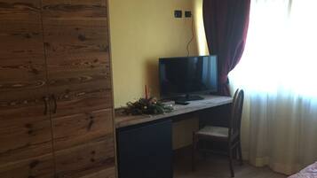 Un dormitorio con un armario de madera, un escritorio con televisor, una silla y una cama con colcha estampada.