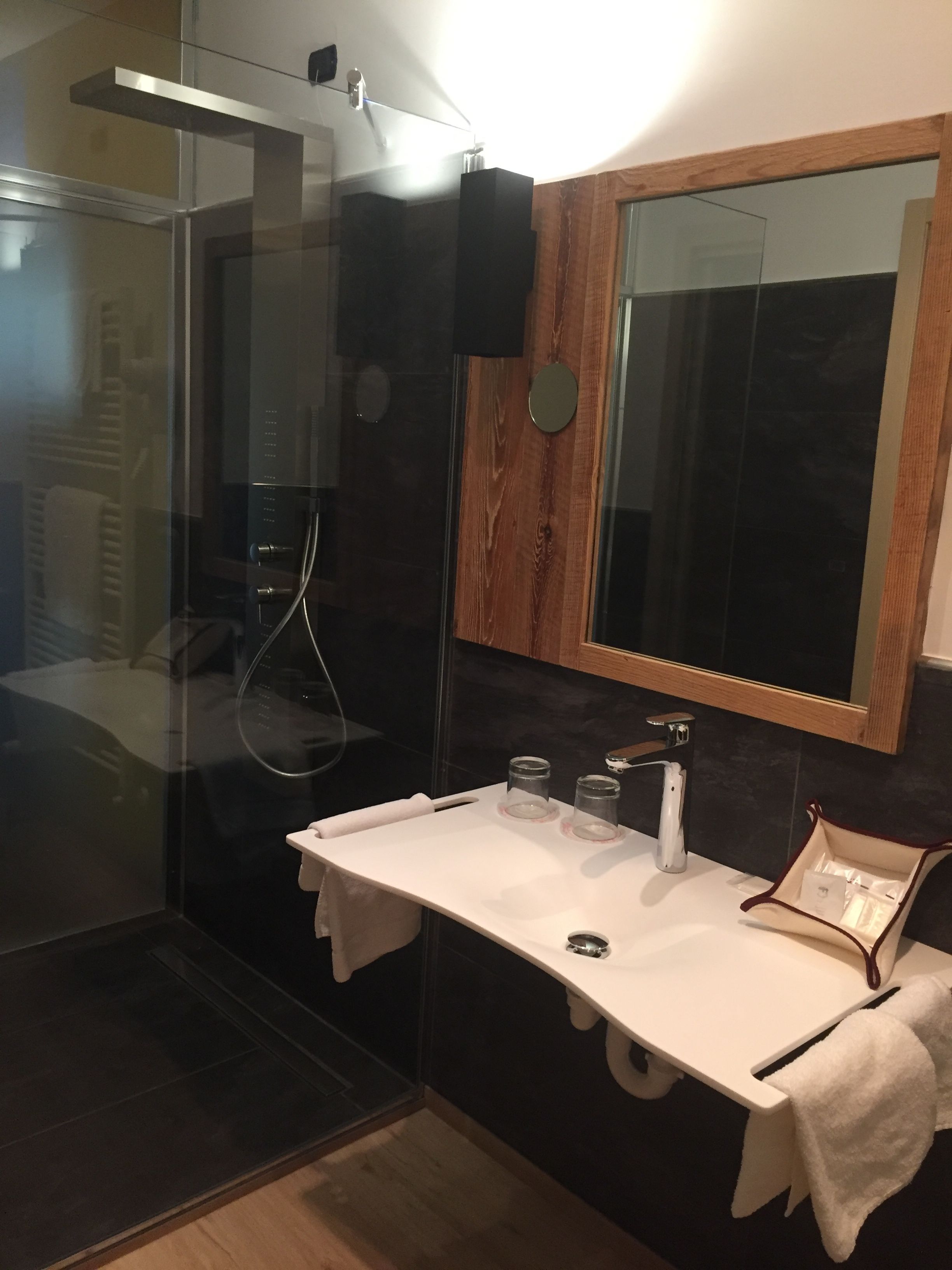 A modern bathroom with a glass-enclosed shower, a white sink with a mirror above it, and a wooden vanity.
