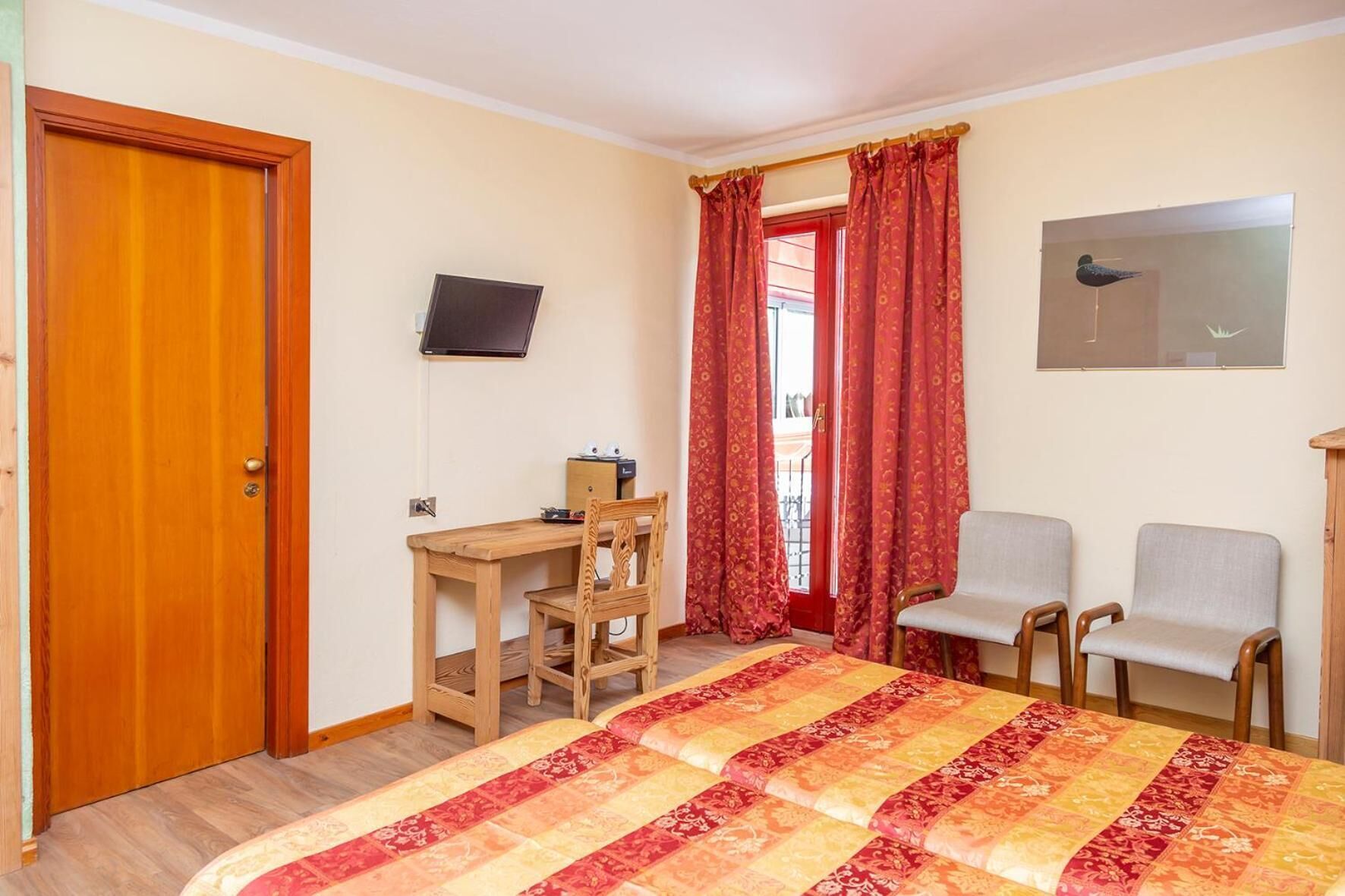 A bedroom with a bed, a desk, two chairs, a TV, and a window with curtains.