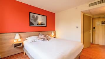 Une chambre d’hôtel comprenant un lit, deux lampes de chevet, une table de chevet, un tableau accroché au mur et une porte donnant sur une autre pièce.