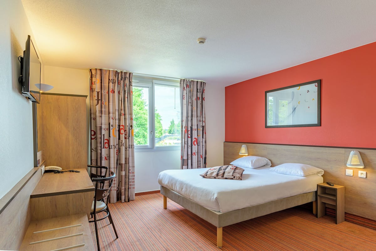 A hotel room with a bed, a desk, a chair, a TV, and a window with curtains.
