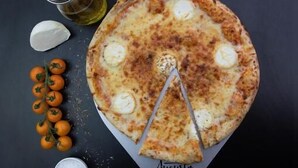 A pizza with a slice missing, surrounded by tomatoes, garlic, and a bottle of oil on a dark surface. - ACE Hôtel Paris Roissy (Mitry-Mory)