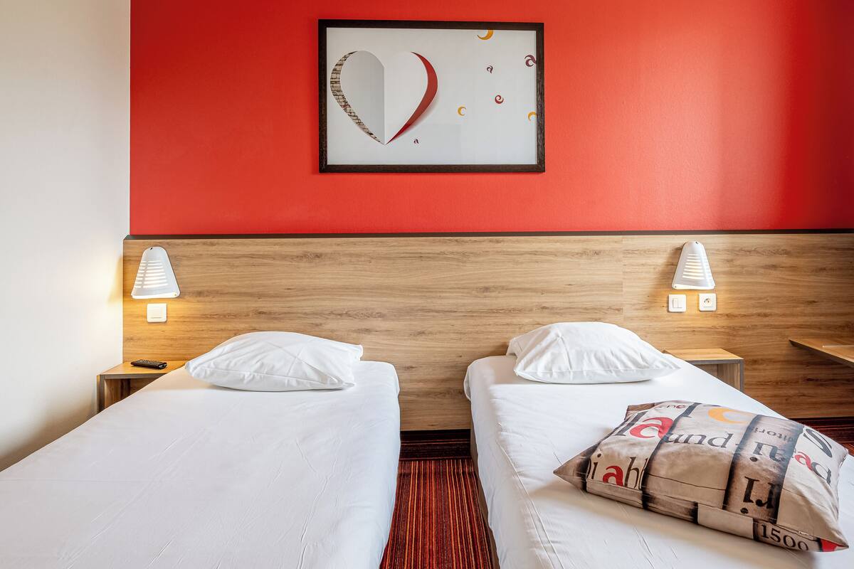 Habitación de hotel con dos camas, una pared roja y una obra de arte enmarcada sobre las camas.