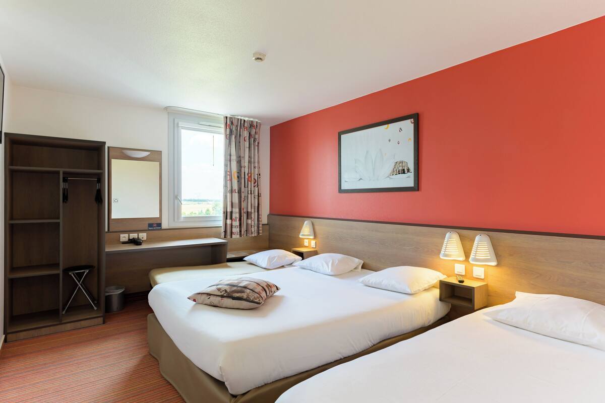 Habitación de hotel con dos camas, un armario, una ventana con cortinas, un cuadro en la pared y lámparas de noche.