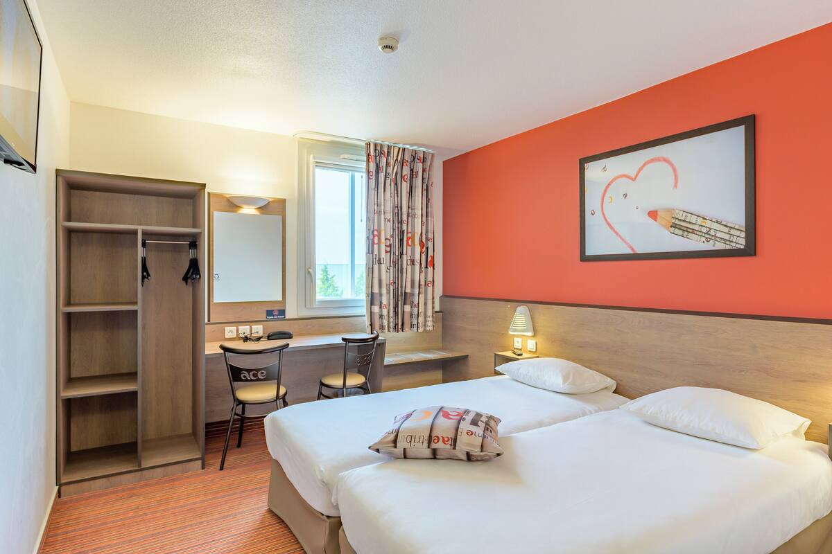 A hotel room with a bed, a desk, a chair, a wardrobe, and a window with curtains.