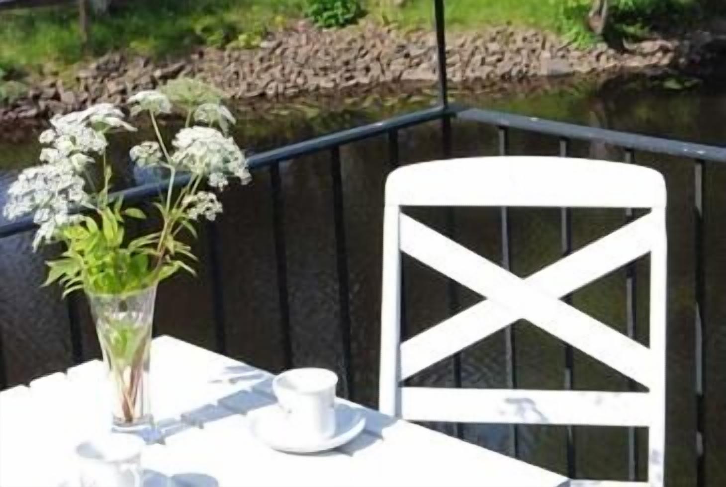Una mesa con una silla y una taza blancos, y un jarrón con flores.