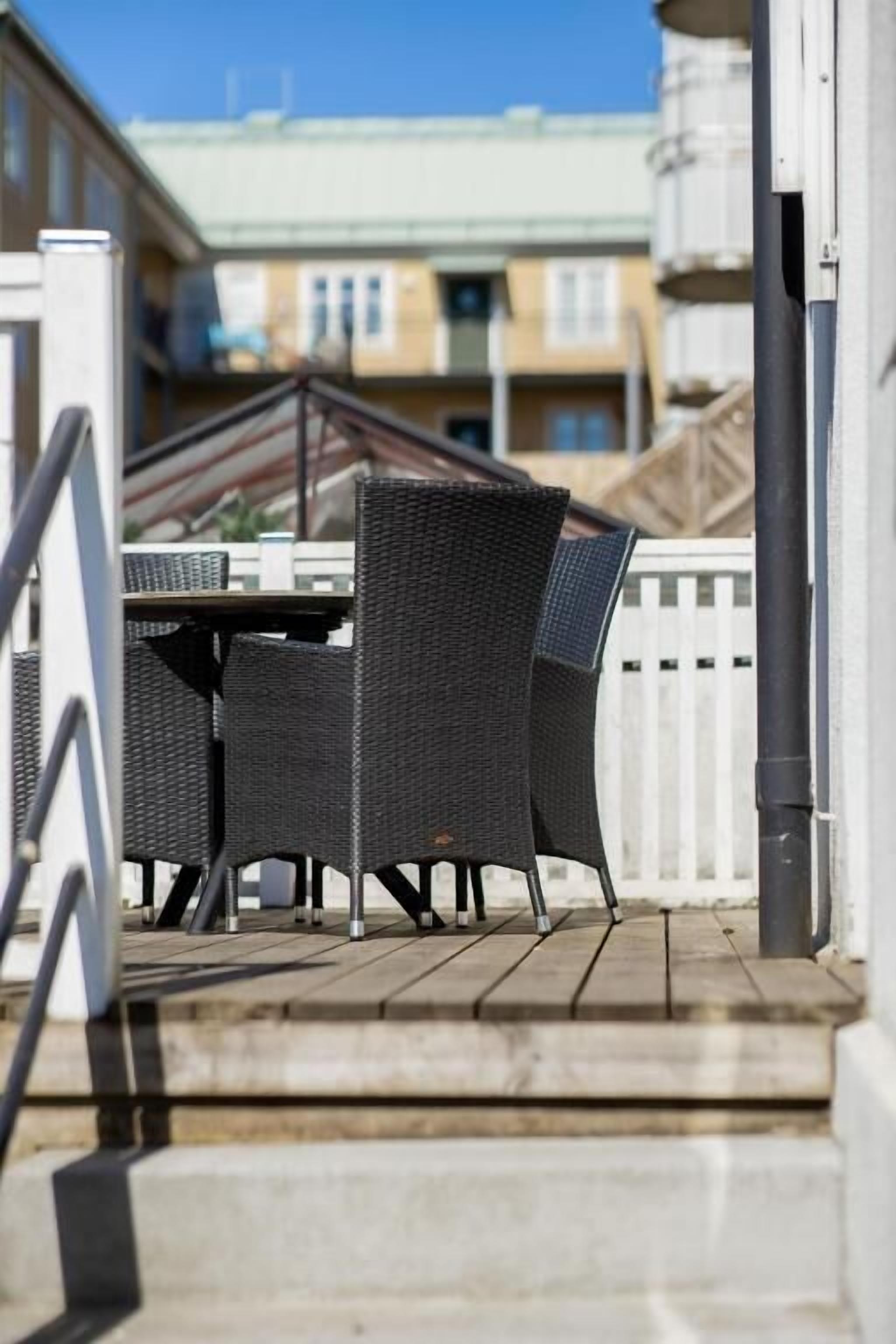 A wooden deck with outdoor furniture, a white fence, and buildings in the background.