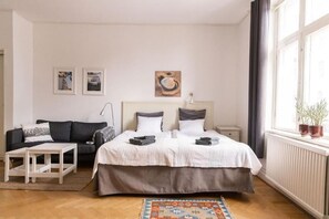 A bedroom with a bed, a bedside table, a sofa, and a window with curtains. - Hotell Villa Rönne (Angelholm)