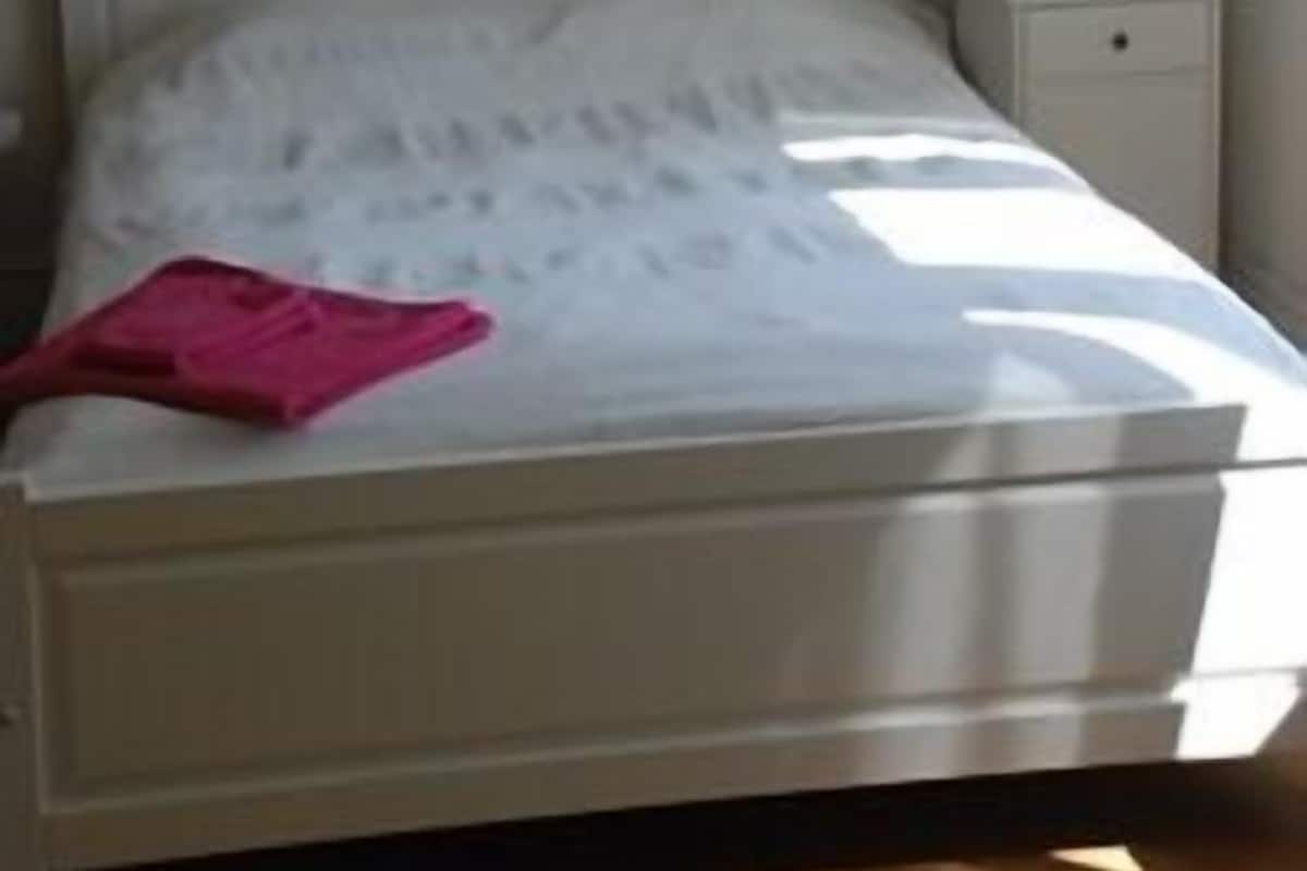Un dormitorio con una cama blanca, una mesita de noche con lámpara y un cuadro en la pared.