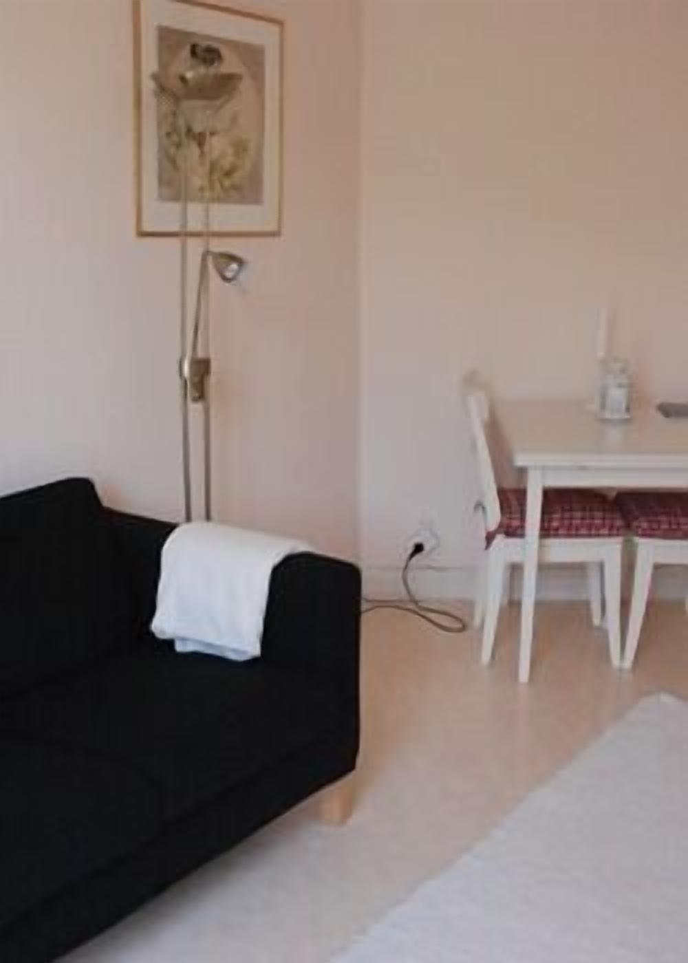 Una habitación con un sofá negro, una mesa blanca con mantel a cuadros rojo y blanco, y un cuadro en la pared.