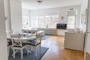 A room with a dining table and chairs, a radiator, a television, and a window with a view of trees. - Hotell Villa Rönne (Angelholm)
