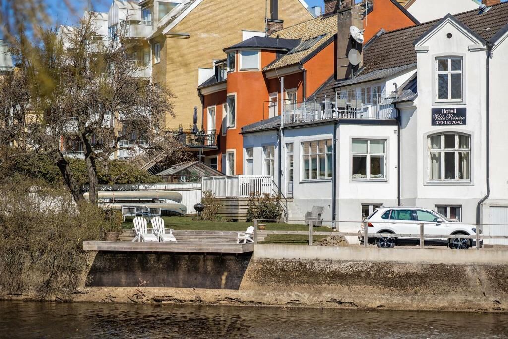 Ett hotell vid vattnet med ett poolområde, en vit bil parkerad framför och en byggnad med balkonger.