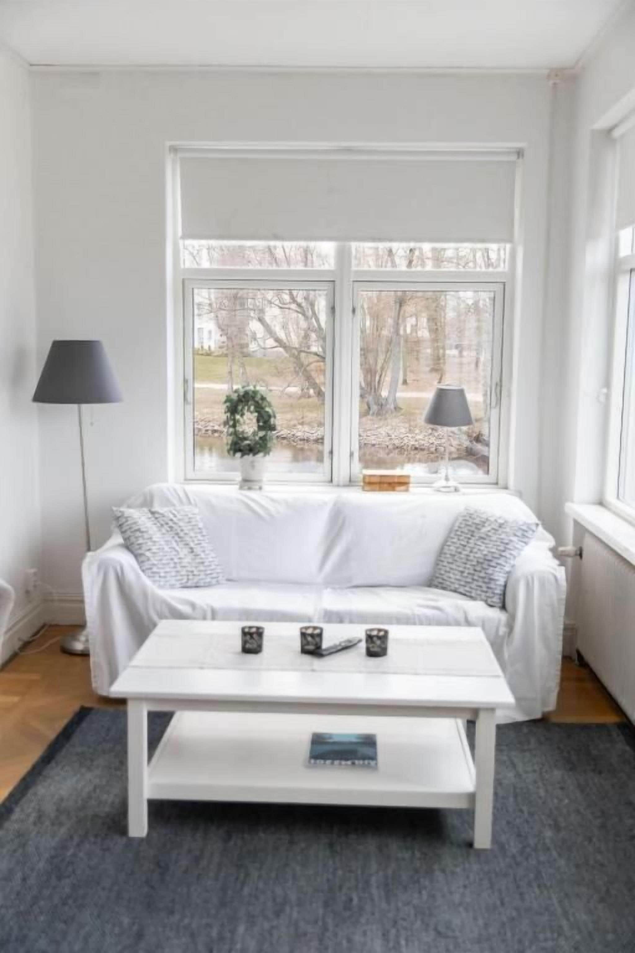 A room with a white sofa, a white coffee table, and a window with a view of trees.