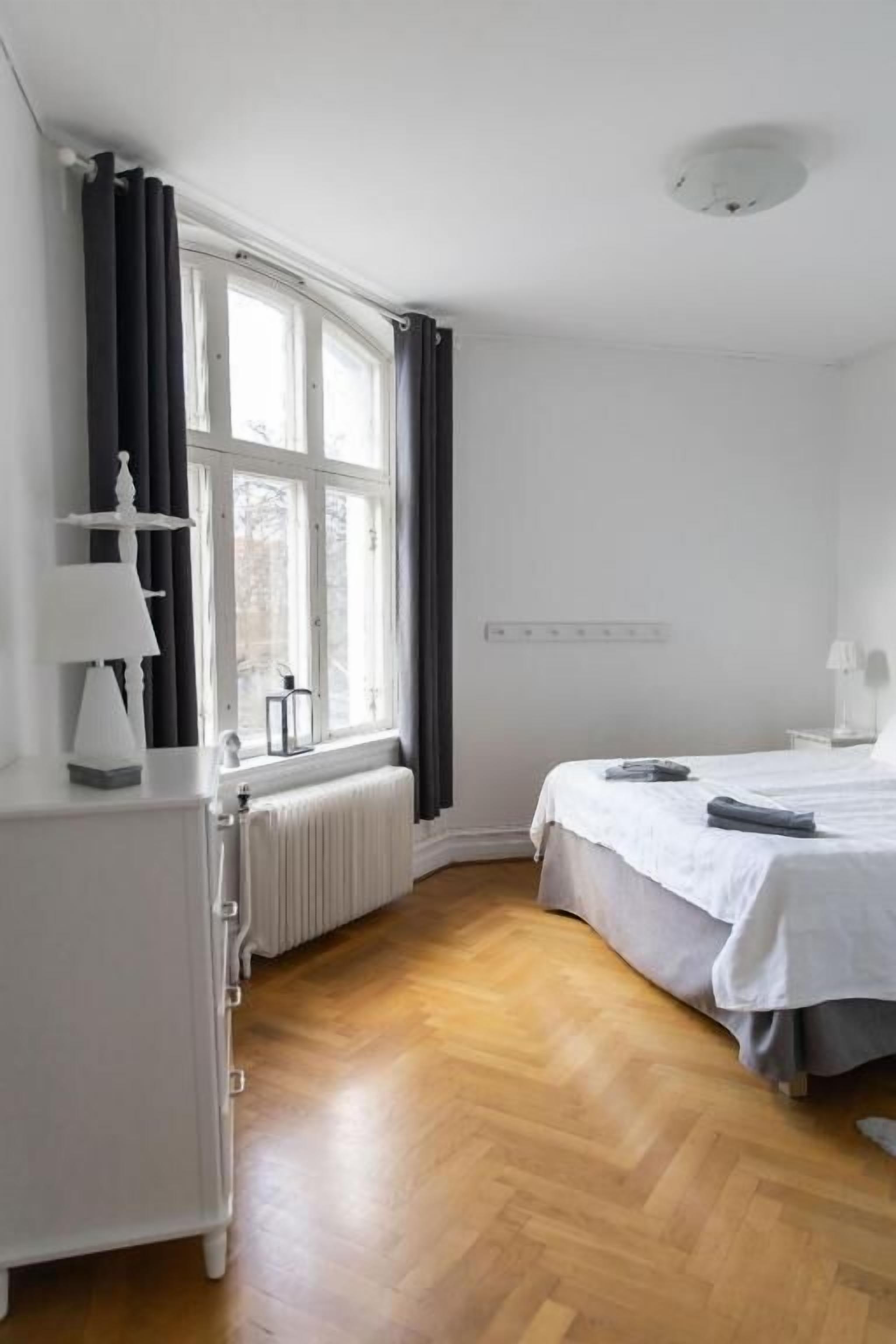 A bedroom with a bed, a radiator, a window with curtains, and a white dresser.