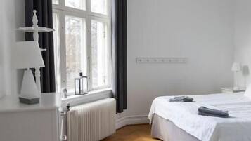 A bedroom with a bed, a radiator, a window with curtains, and a white dresser.