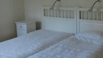 A bedroom with a double bed, a nightstand, and a wall-mounted shelf.