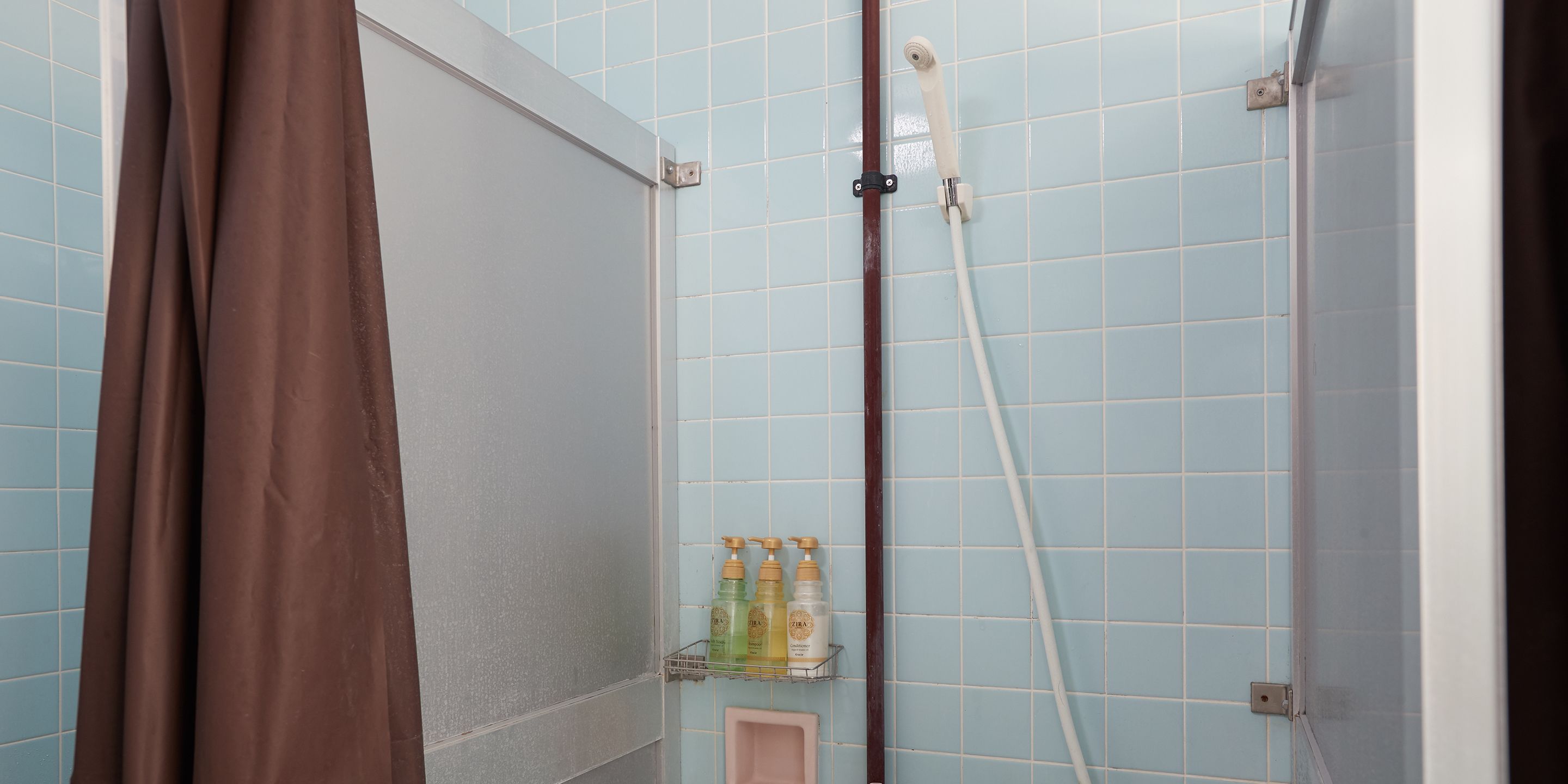A bathroom with blue tiles, a shower, a brown curtain, and a shelf with toiletries.
